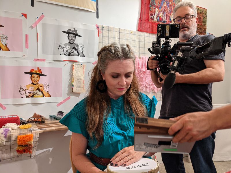 Margaret Timbrell embroidering in her studio during filming for Handcrafted Hotels, with Minnie Pearl reference photos on the wall behind her